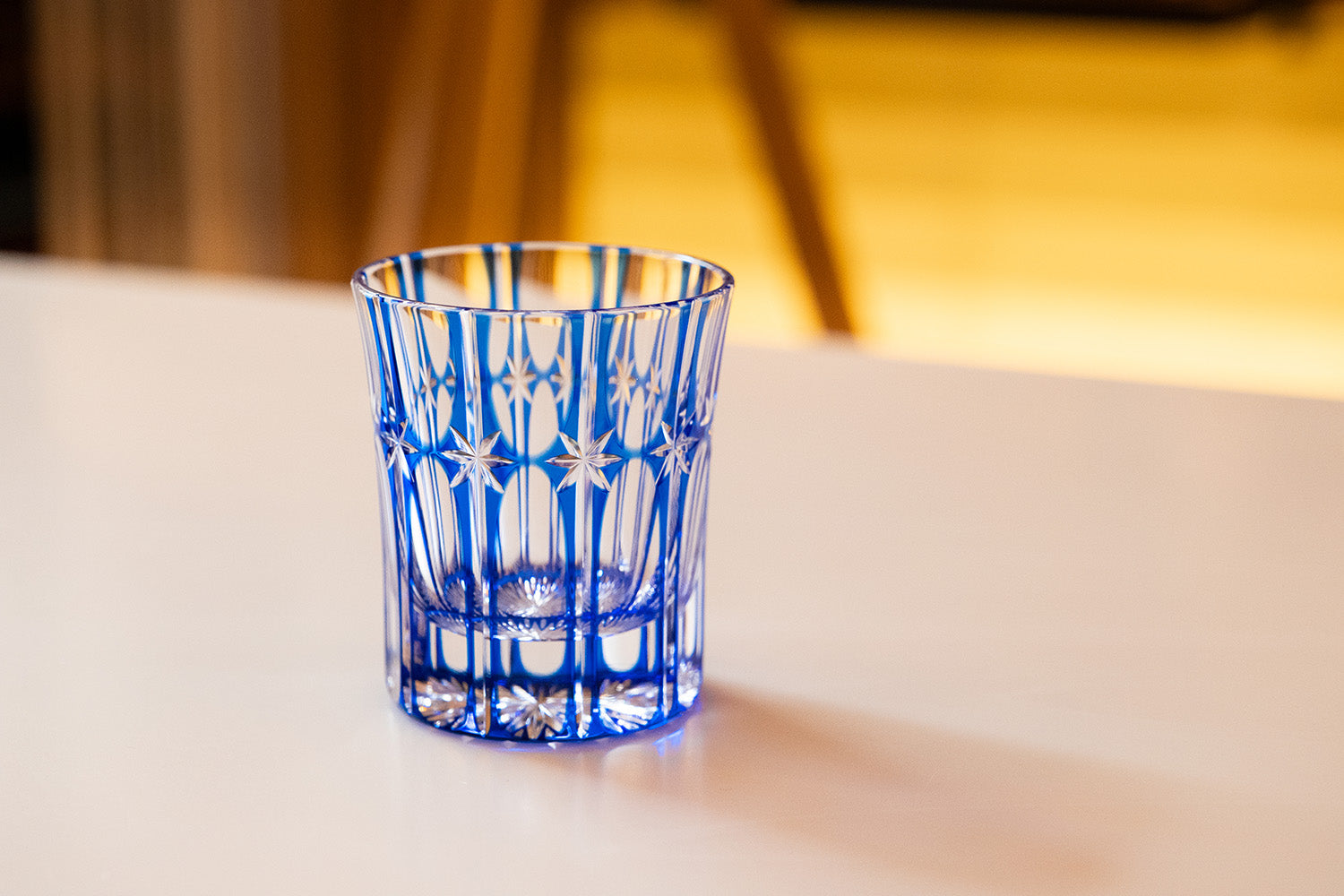 A blue Temma Kiriko glass with intricate star and vertical cut patterns, sitting on a white tabletop.