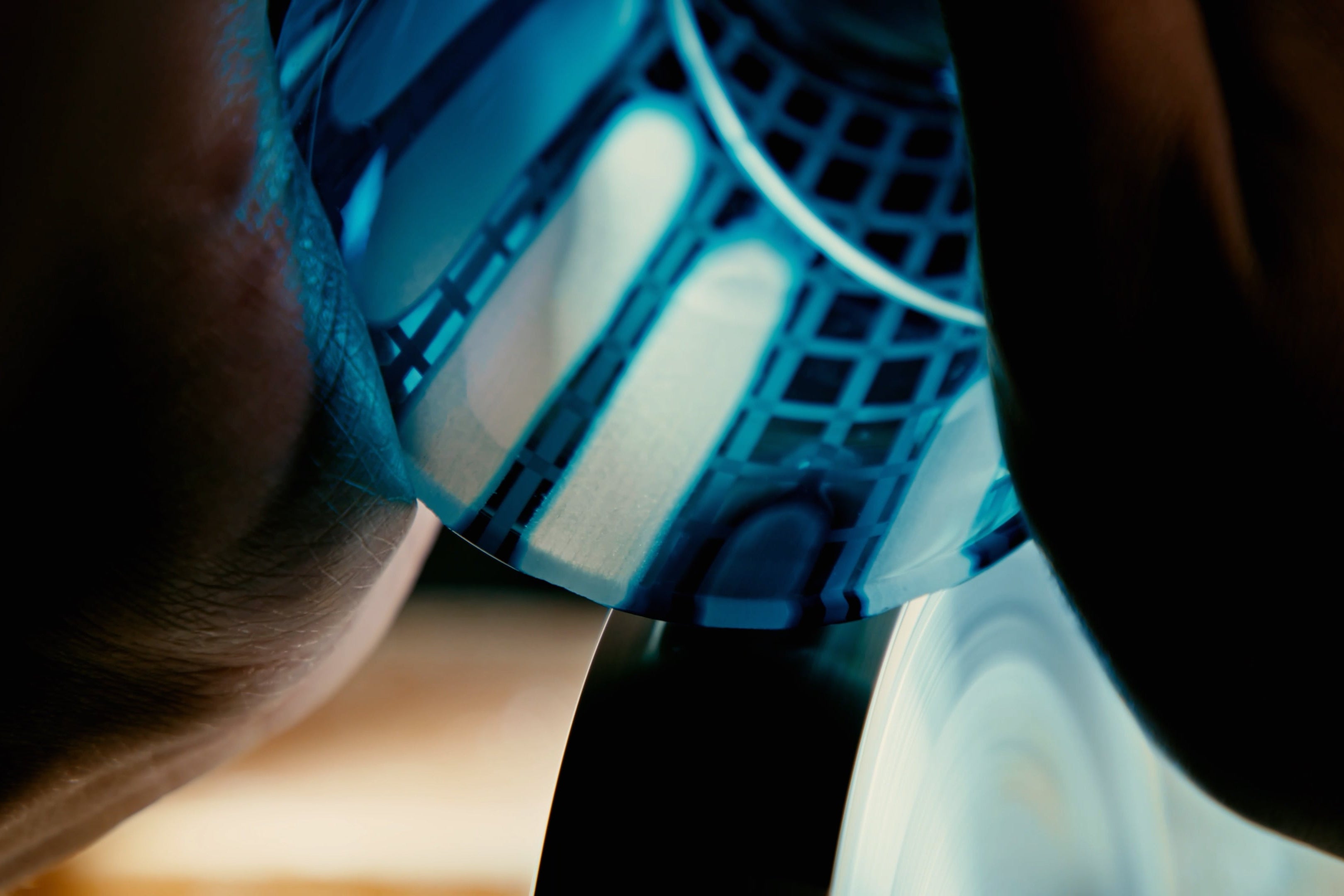 A light blue glass is being cut by an artisan on a mechanical wheel
