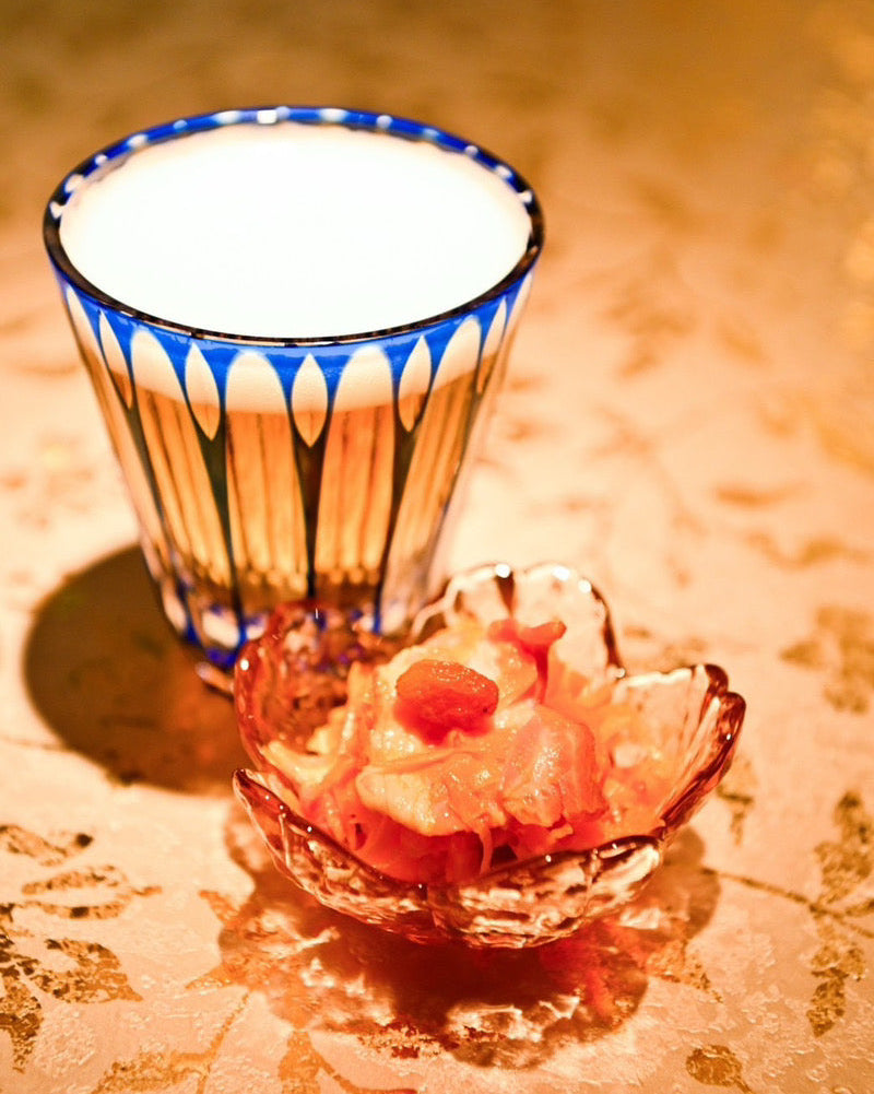 There are Temma Kiriko's SHIZUKU Crystal Tumbler glass wit the beer inside and the small food on the side on a table